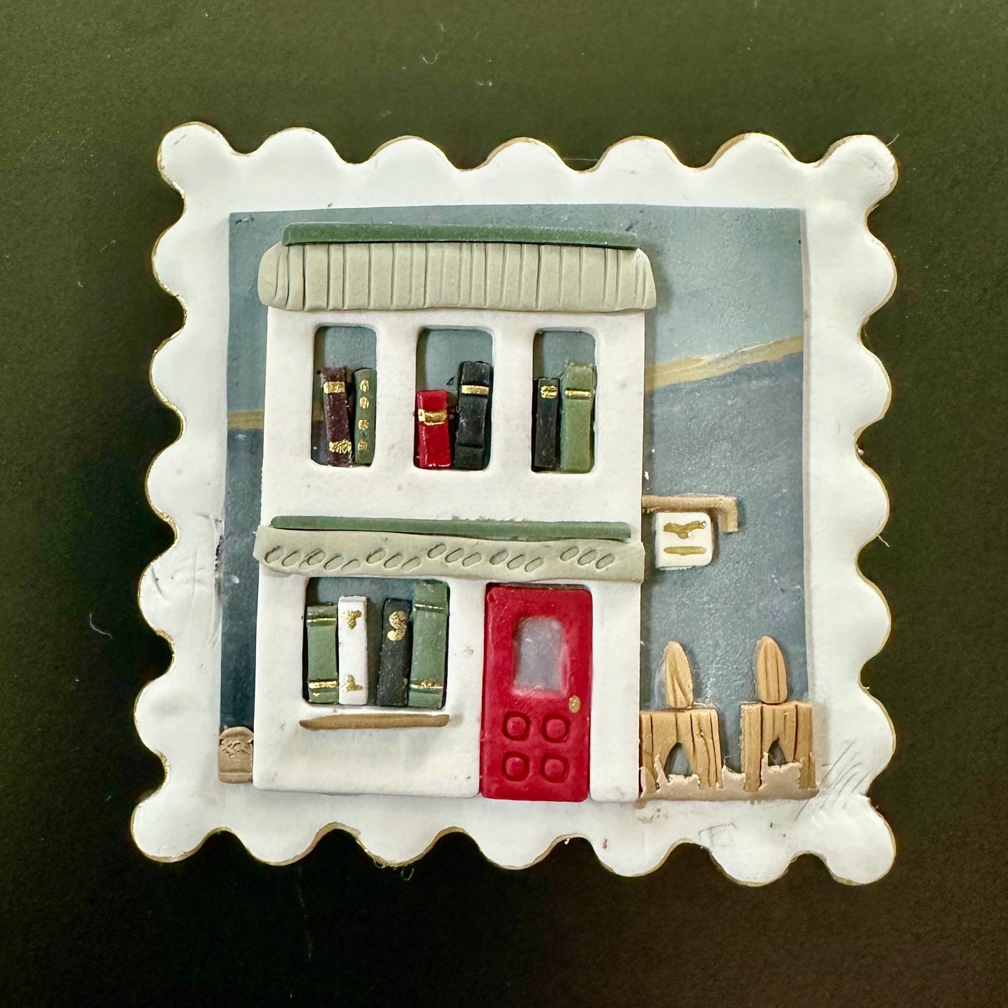 Decorative brooch of a small bookstore on the shorefront with a red door. Available as wall art, magnet or brooch.